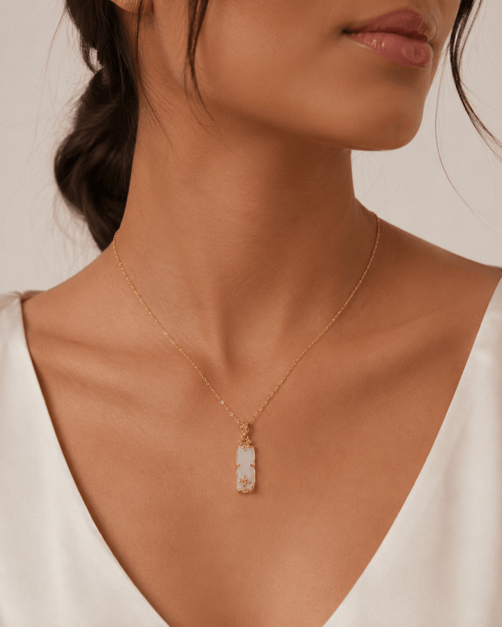 Gold-plated pendant necklace worn at the neckline, showing the white rectangular charm